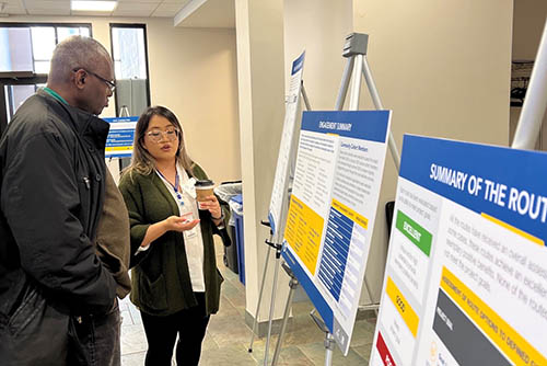 Two people talking while looking at poster boards with route information.