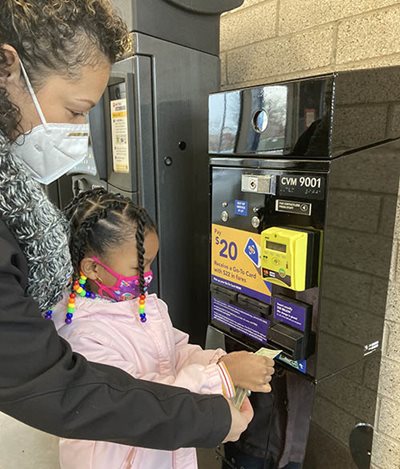An adult and child adding a bill to a ticket machine.