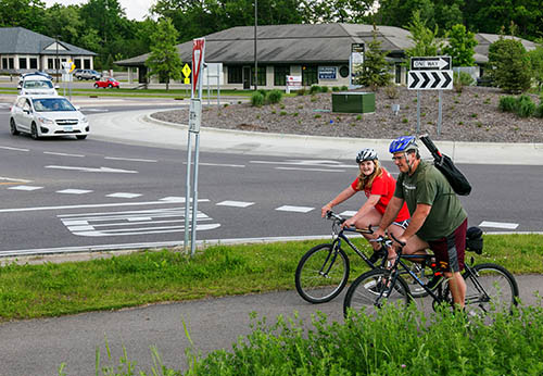 Bikers on a paved path and cars in a roundabout.