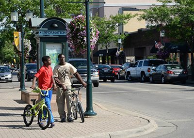 Two people with bikes waiting to cross a street.