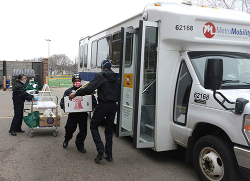 Two workers loading a box of groceries onto a Metro Mobility vehicle.