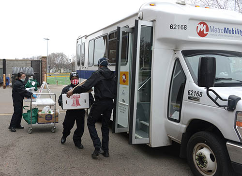 Workers in masks loading boxes of food onto a Metro Mobility vehicle.