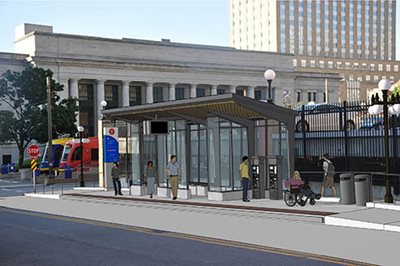 A bus station with people waiting, next to the Union Depot with a Green Line train.