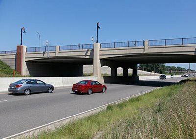 Two cars driving toward a bridge over the divided highway.