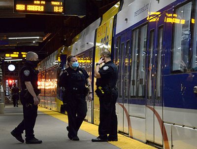 Three police officers in masks next to a train at a station platform.