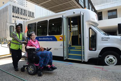 A bus driver helps a woman in a wheelchair next to a bus.