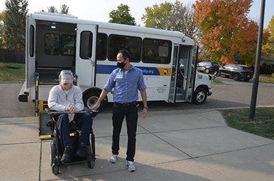 A Metro Mobility driver accompanies a passenger from the bus.