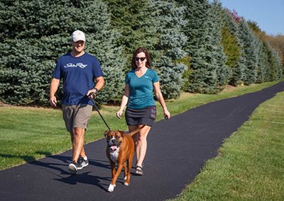 Two people and their dog walking on a paved trail.