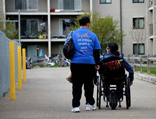A person walking next to a person in a wheelchair.