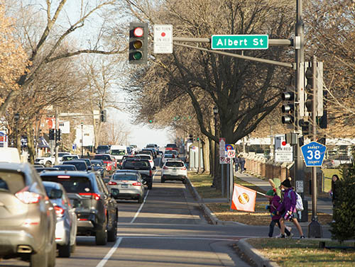 Cars in traffic on a busy street. Children are preparing to cross the road.