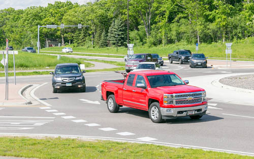 Two trucks and a car inside a roundabout, with more vehicles waiting to enter.