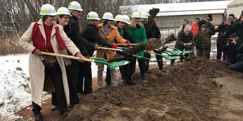 10 people digging and tossing dirt with green shovels.