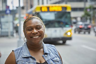 A smiling transit customer with a bus in the background.
