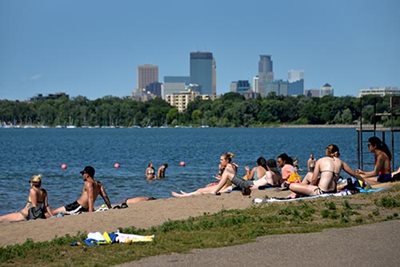 A few people in the lake and several people on the beach on a sunny summer day.