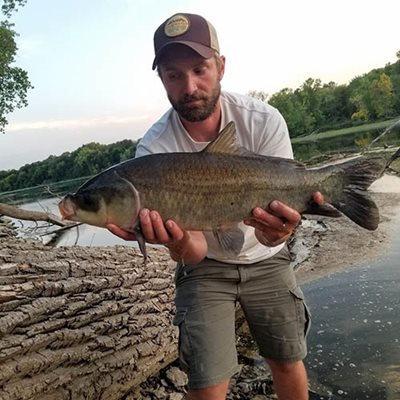 Tyler holding a fish at the edge of a river.