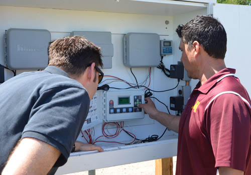 University researcher Jonah Reyes (right) shows one of the irrigation controllers that is part of the U’s irrigation demonstration project.