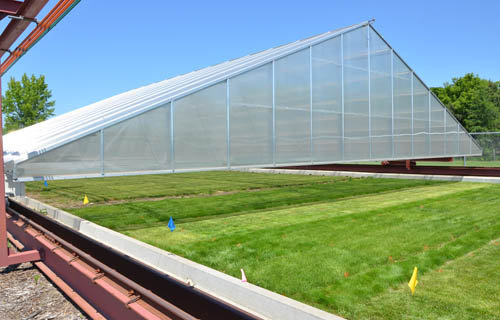 The greenhouse structure travels on rails to cover the test plots when a sensor on its roof detects rain.