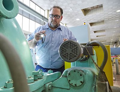 A worker pointing a small flashlight at a large machine.