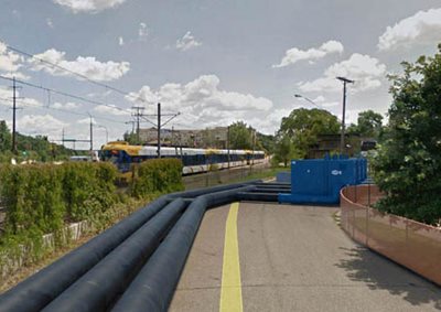 Pipes on a paved road, near a light rail train.