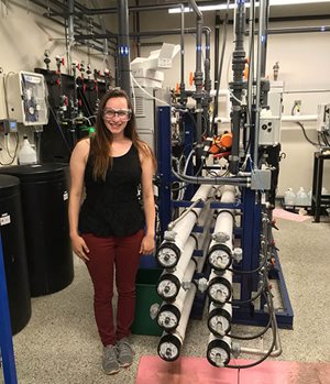 Intern with safety glasses posing next to water equipment.