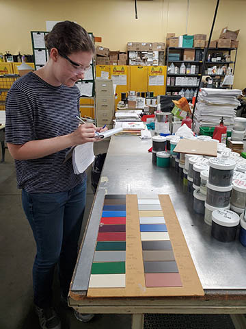 An intern with a notepad standing at a table with color samples and paints.