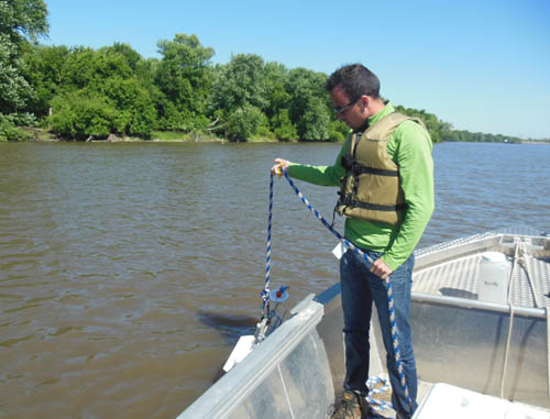 A man standing in a boat holding a rope with testing equipment.