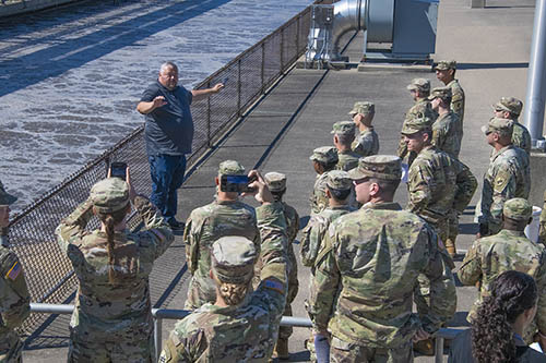 A man explaining the water treatment plant to a group of soldiers in uniform.