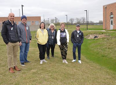 6 people posing in grass near buildings.