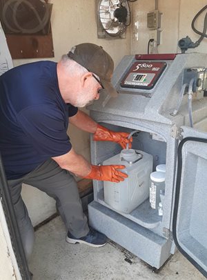 A Metro Plant lab technician removes a plastic carton from an automatic wastewater sampler equipment.