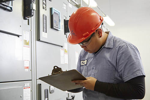 A person in an orange hard hat with a clipboard.