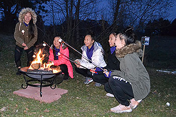 5 people roasting marshmallows over a campfire.
