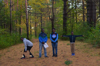 Four youth posing in front of pine trees.