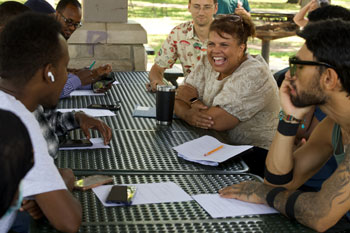 A group of people talking and laughing at three picnic tables that are pushed together.