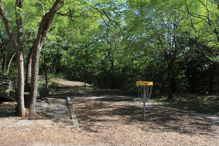 A disc golf target in a wooded park, surrounded by woodchips.