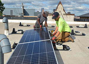 Two people installing solar panels on a flat roof.
