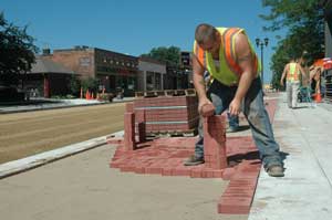 A worker laying bricks on a sidewalk.
