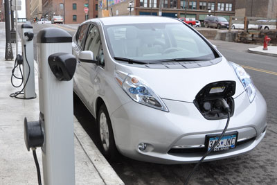 An electric vehicle plugged in while parked along a sidewalk.
