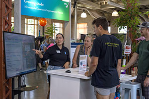 Minnesota Green Corps member and Met Council data scientist interact with two members of the public at the Growing Shade booth of the State Fair.