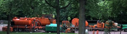 Photo of sewer cleaning equipment and trucks parked on a tree-lined street