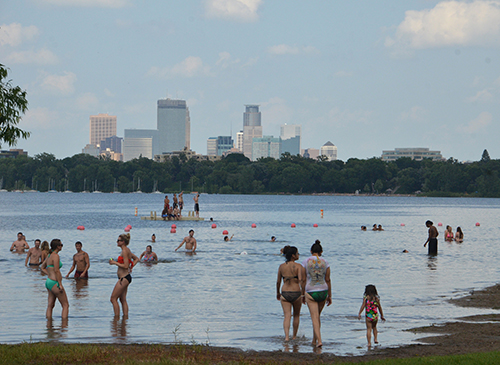 Swimmers at a lake, with the Minneapolis skyline in the background.