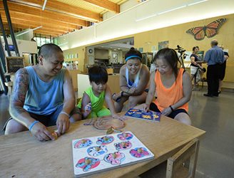 Smiling man, boy and two girls at indoor table at regional park