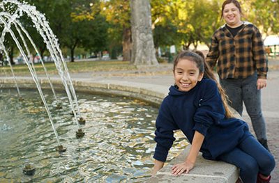 Child touches water in large fountain while adult looks on