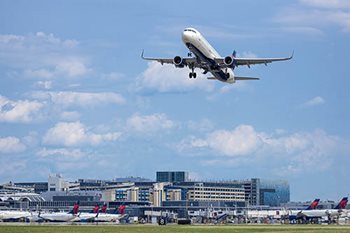 Jet is in the air above Terminal 1 and many jets parked at gates.
