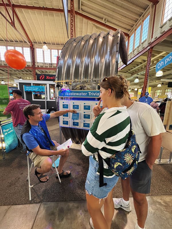 Visitors challenge themselves with the wastewater trivia quiz. A couple ponders the answer to a question as a Met Council volunteer picks the next one.