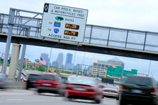 Blurry vehicles underneath a carpool rate sign.